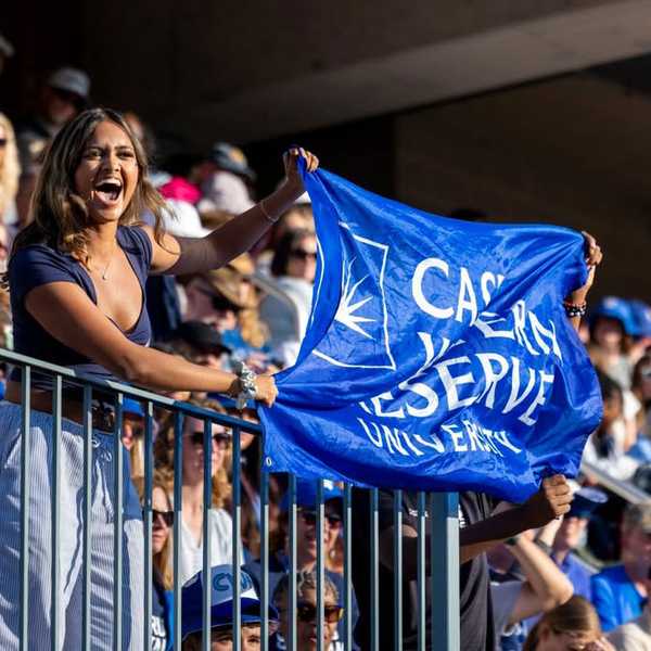Student holding a flag that reads, “Case Western Reserve University," in the crowded stands of DiSanto Field.