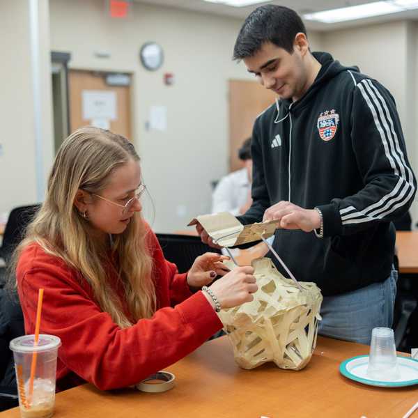 Two CWRU students building a protective structure for a lightbulb drop competition.