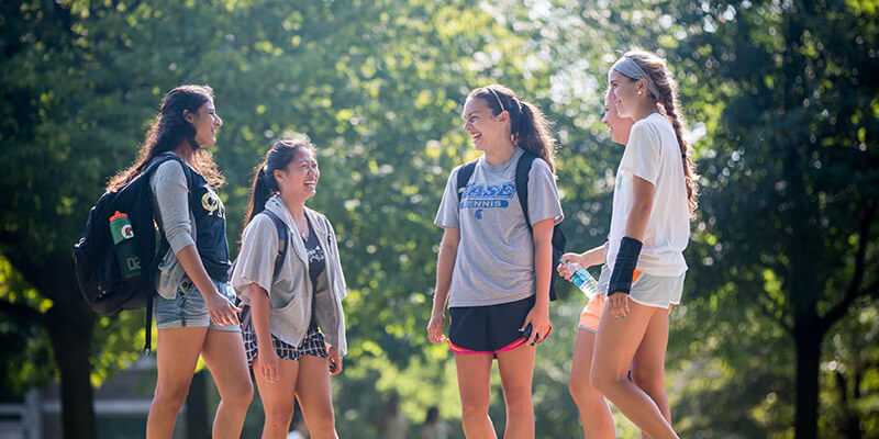 Photo of a group of Case Western Reserve University students standing in a circle outdoors on the quad, laughing