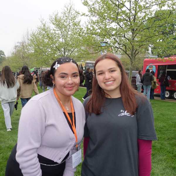 Two students pose on East Bell Commons with a stage and food trucks in the background.